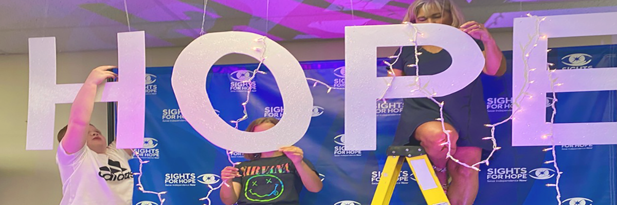Two campers and a counselor hang letters from a ceiling; the letters spell HOPE