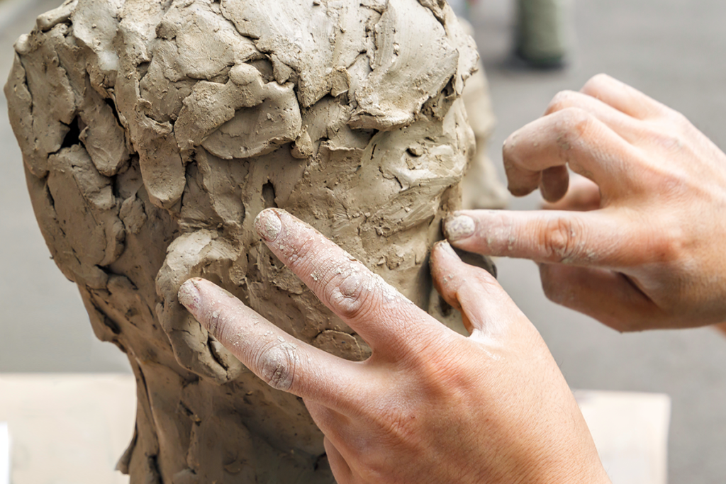 Two hands working on a clay sculpture